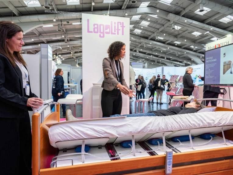 Eine Frau präsentiert ein Krankenbett auf einer Messe.