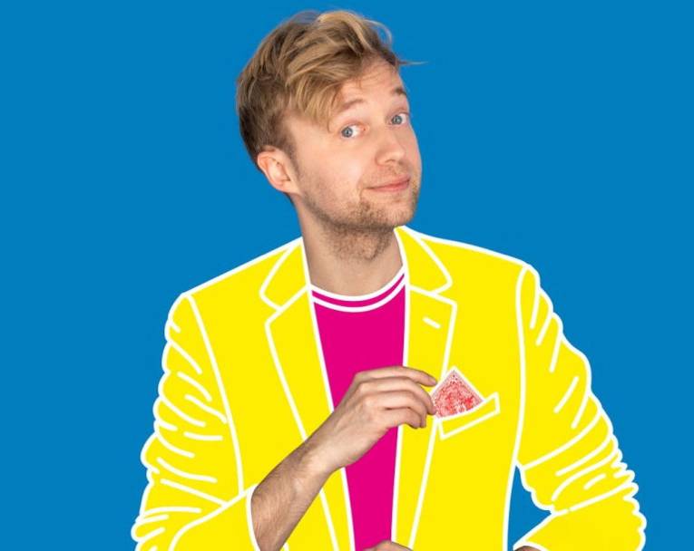 Mann mit kurzem Haar und etwas Bart in aufgemaltem T-Shirt und Jackett greift nach einer Spielkarte in seiner Brusttasche.