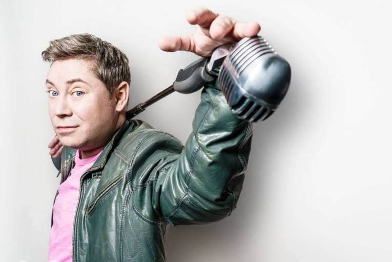 Mann mit kurzem Haar hält ein Stabmikro quer hinter seinen Kopf.