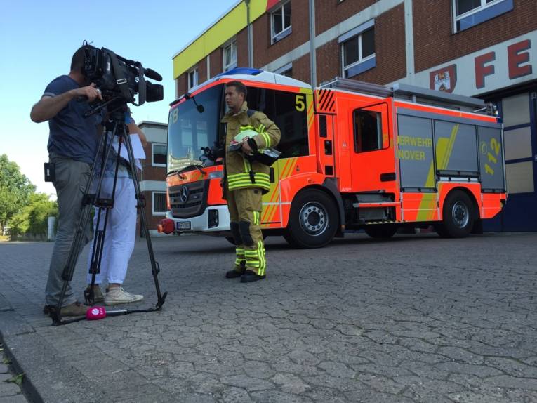 Feuerwehrmann wird von Kamerateam vor einem Feuerwehrauto vor der Wache interviewt