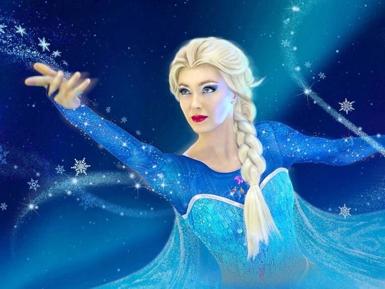 Zu sehen ist eine Schauspielerin als Elsa von „Die Eiskönigin“ von Disney verkleidet. Ihre Hände sind ausgestreckt und glitzernde Schneeflocken umkreisen die Arme und den Körper.