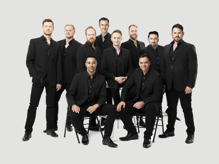 Zu sehen sind zehn Männer in schwarzen Anzügen vor einem weißen Hintergrund.
