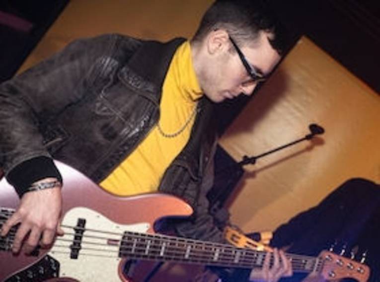 Mann mit kurzem Haar und Brille spielt E-Bass.