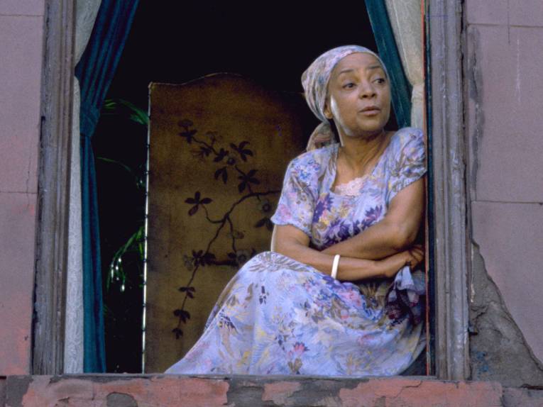 Eine Frau sitzt auf der Fensterbank eines geöffneten Fensters und schaut hinaus.