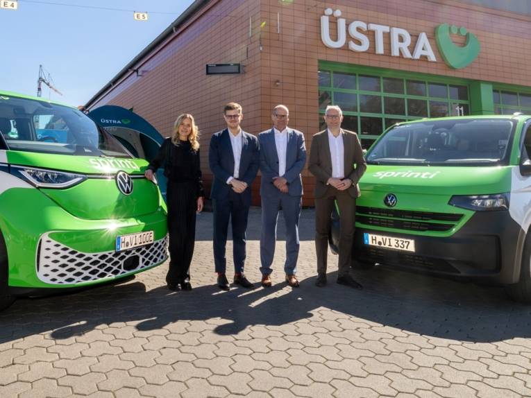 Drei Männer und eine Frau stehen nebeneinander, links und rechts daneben E-Autos von VW mit der Aufschrift "Sprinti".