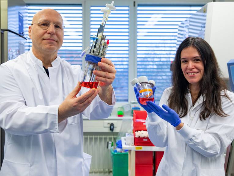 Eine Frau und ein Mann in einem Labor halten Geräte und Behälter mit roter Flüssigkeit in den Händen.