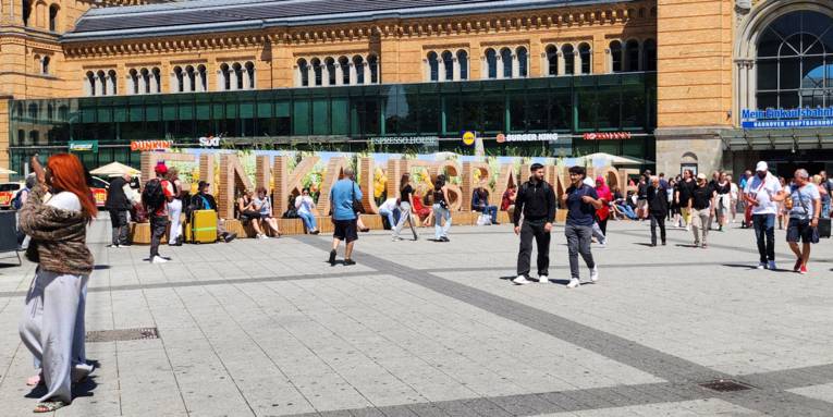 Holz-Sitzelemente vor dem Hauptbahnhof Hannover, die das Wort Einkaufsbahnhof ergeben.