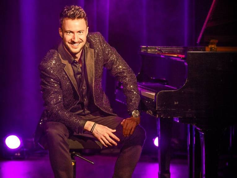 Lächelnder Mann mit kurzem Haar sitzt vor einem Klavier.