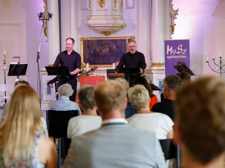 Zwei Künstler tragen in einer Kirche vor Publikum vor.