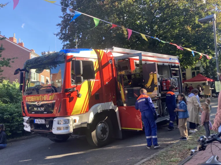 Das EInsatzfahrzeug der Feuerwehr und Wimpelkette. Sowie zwei junge Menschen der Jugendfeuerwehr und Besuchende