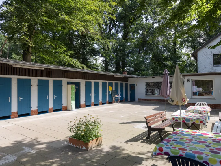 Geb&auml;ude mit blauen Holzt&uuml;ren, davor eine Terrasse mit Tischen und B&auml;nken/St&uuml;hlen