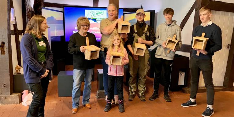 Sieben stehen in der Infoscheune Naturpark Steinhuder Meer und halten Vogelh&auml;uschen in die Kamera.