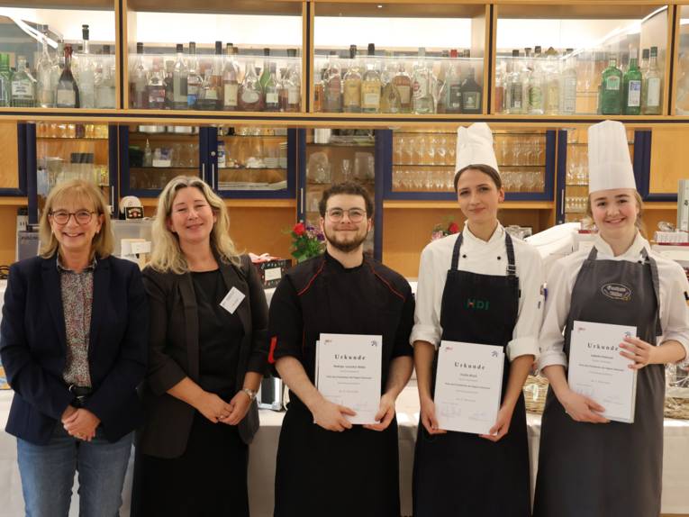 Fünf Personen, drei davon halten eine Urkunde in der Hand