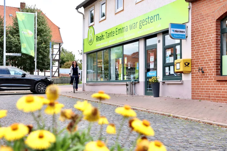 Laden mit Schild über dem Ladeneingang auf dem steht: Rnah: Tante Emma war gestern, davor Straße und eine Radfahrerin
