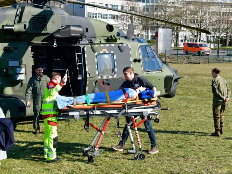 Medizinisches Personal mit einem Menschen auf einer Trage vor einem Militärhubschrauber