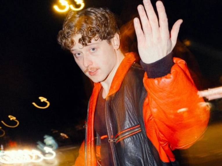 Mann mit kurzen Locken und Oberlippenbart und erhobener linker Hand