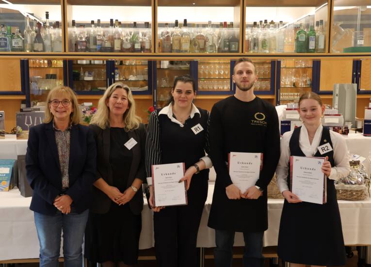 Fünf Personen, drei davon halten eine Urkunde in der Hand