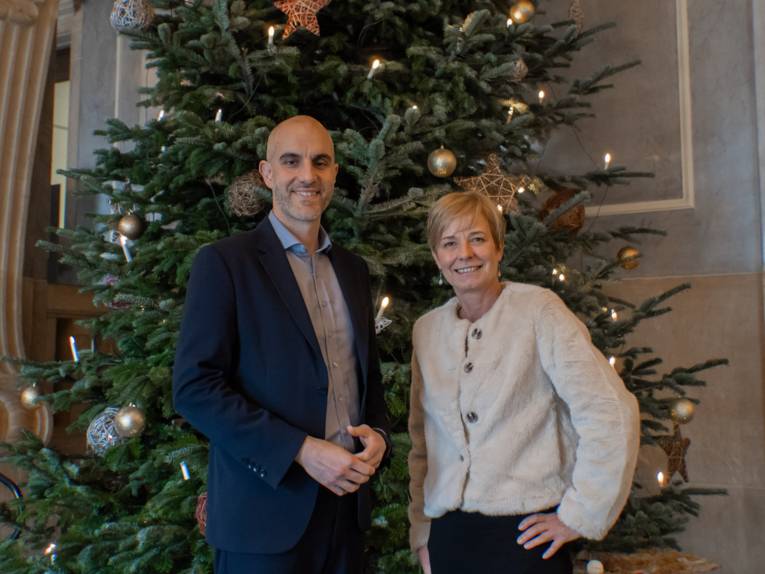 Zwei Personen stehen vor einem großen Weihnachtsbaum.