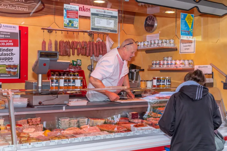 Ein Verk&auml;ufer bietet einer Kundin seine Wurst- und Fleischwaren an.