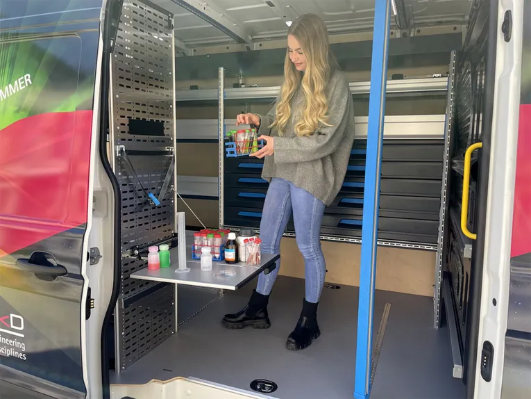 Junge Frau steht in einem Transporter, dessen Innenraum zu einem Labor umgebaut ist.