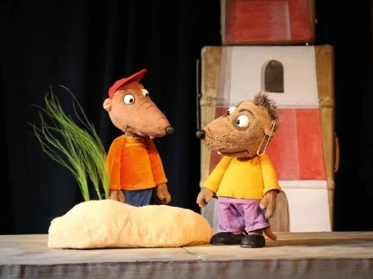 Zwei Ratten-Puppen stehen vor einem Leuchtturm auf der Bühne.