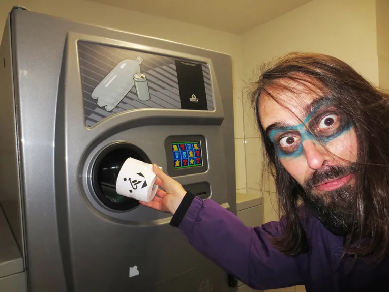 Ein maskierter Mann steckt  eine Toilettenpapierrolle in einen Dosenpfandautomat