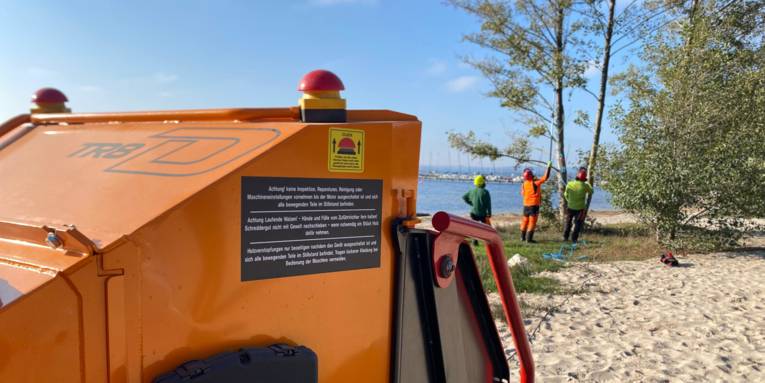 Blick &uuml;ber einen mobilen H&auml;cksler zu Personen, die in der Ferne B&auml;ume begutachten.