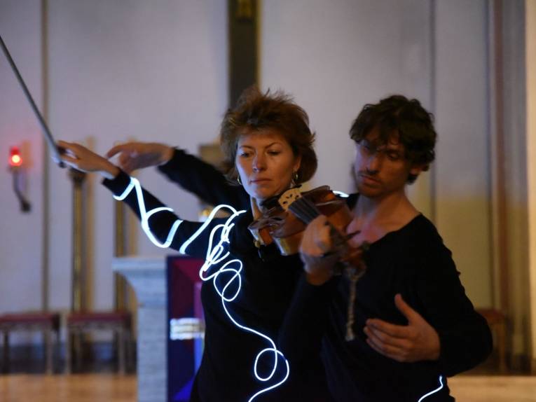 Eine Frau mit Violine und ein Mann hinter ihr