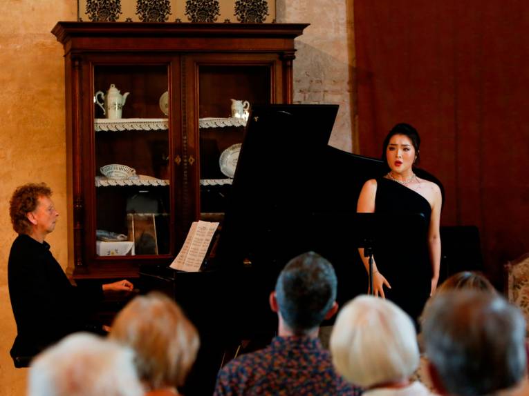 Ein Mann spielt auf einem Piano, eine Frau steht daneben und singt dazu.