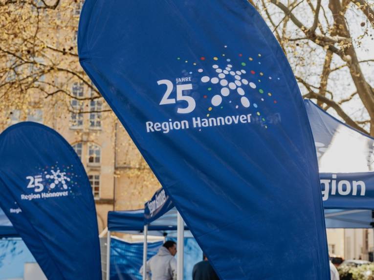 Eine Beachflag in der Mitte des Bilds mit Aufschrift "25 Jahre Region Hannover", im Hintergrund Pavillons und weitere Beachflags.
