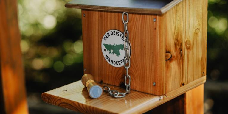 Holzkasten, an dem mit einer Kette ein Stempel befestigt ist