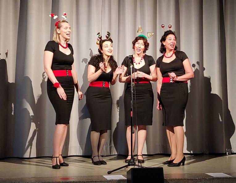 Vier Frauen mit engen Röcken, ausgeschnittenen Shirts, buntem Kopfschmuck und Pumps auf einer Bühne