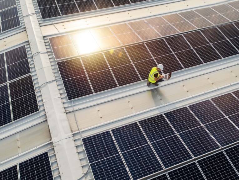 Blick auf eine Dachlandschaft voller Solarfelder. Darauf ein Monteur.