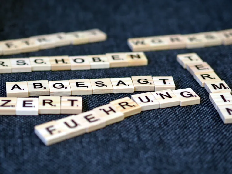 Holzplättchen mit Buchstaben bilden verschiedene Worte. Das Wort "Abgesagt" ist scharf lesbar, während andere Worte unscharf sind.