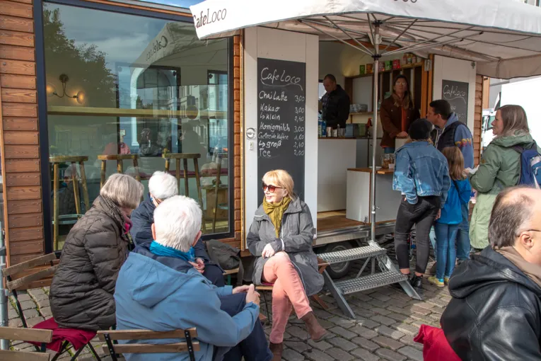 Menschen sitzen in einem Stra&szlig;encaf&eacute; auf dem Wochenmarkt.