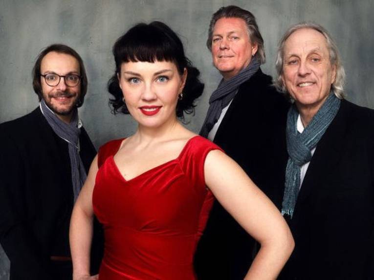 Vorne eine Frau mit Trägerkleid, hinten drei Männer mit Jacketts und Halstüchern