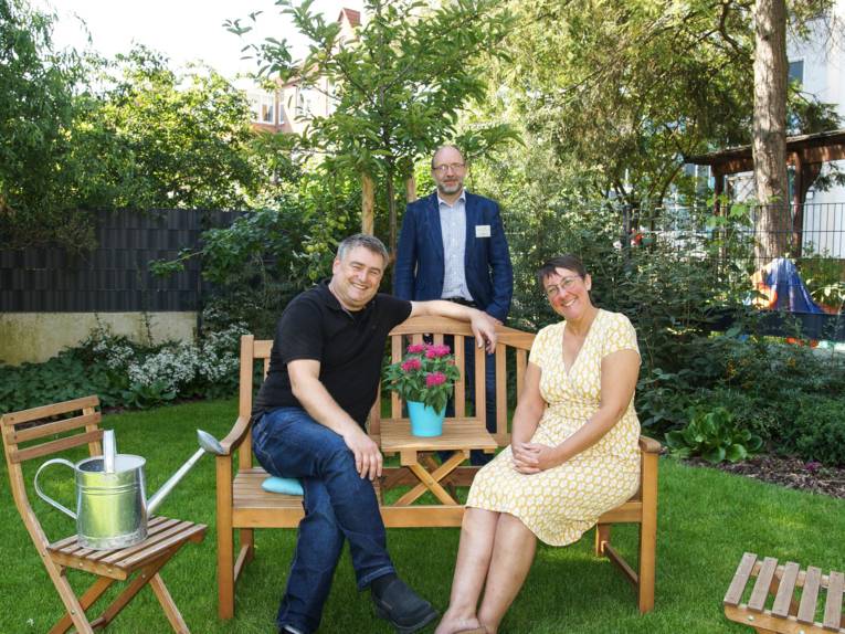 Drei lächelnde Personen in einem Garten.