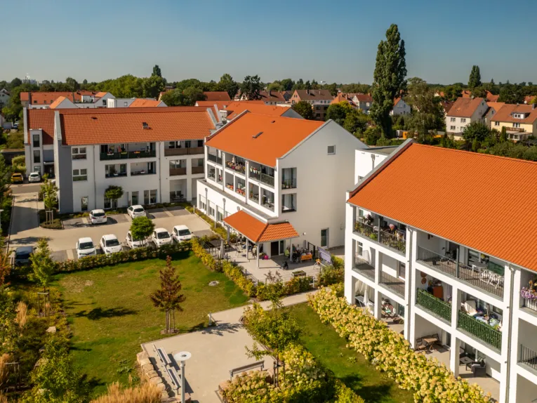 Blick auf mehrere neu gebaute Mehrfamilienhäuser mit roten Dachziegeln, Balkonen und Parkplätzen.