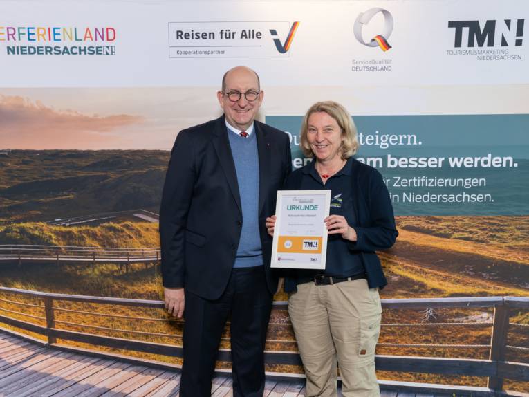 Zwei Personen stehen nebeneinander, eine hält eine Urkunde in den Händen.