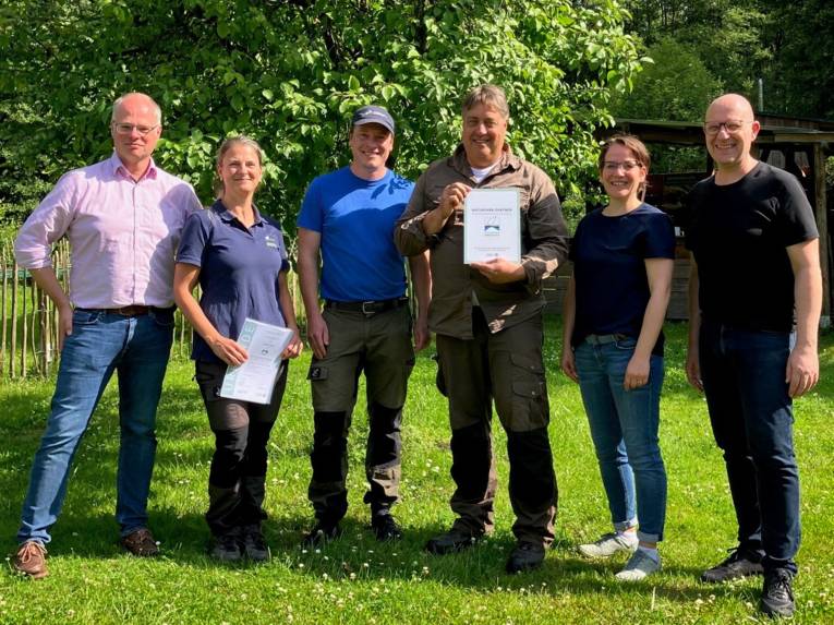 Sechs Personen stehen nebeneinander, zwei Personen halten Urkunden