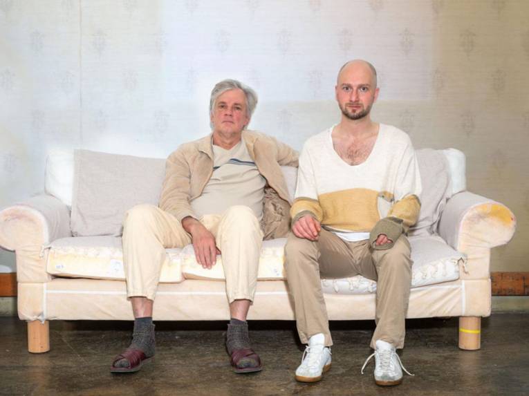 Zwei Männer sitzen auf einem Sofa.