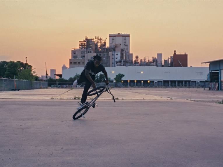 Zu sehen ist ein Film Still aus „Mr. Cato“: Ein Biker zeigt einen Strick mit dem Fahrrad vor einer untergehenden Sonne.