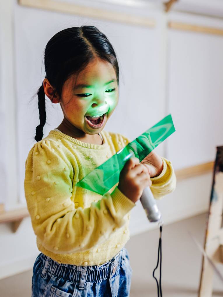 Ein Kind leuchtet mit einer Taschenlampe durch ein St&uuml;ck gr&uuml;ne Folie.