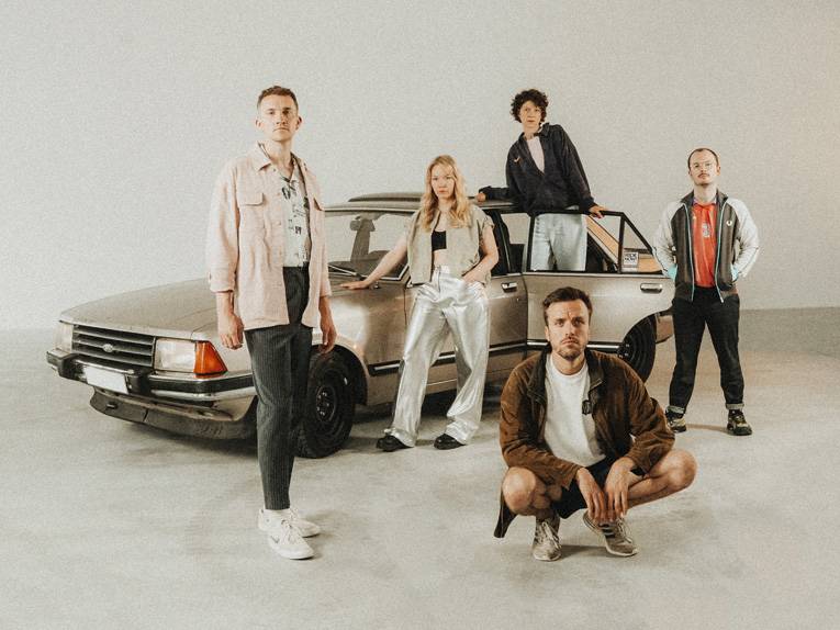 Die fünf Mitglieder der Band „Das Lumpenpack“ posieren vor einem Auto