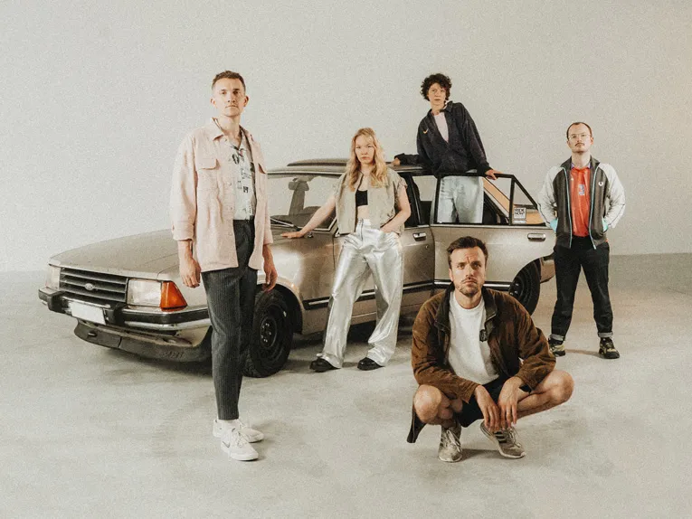Die fünf Mitglieder der Band „Das Lumpenpack“ posieren vor einem Auto