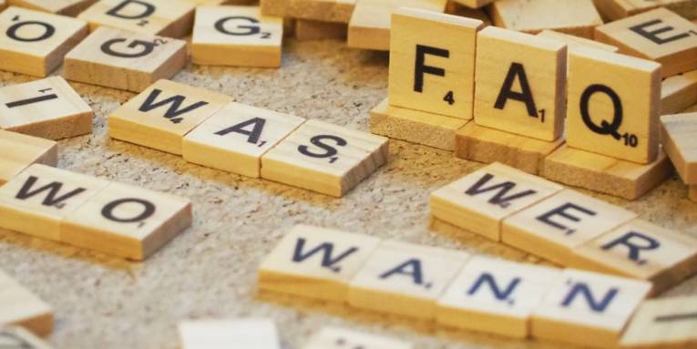 Holzbuchstaben liegen durcheinander, erkennbar sind Frageworte und auf hochkant stehenden Holzplättchen: "FAQ"