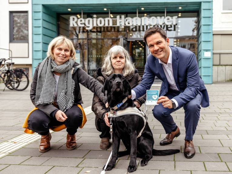Drei Personen gehen in die Hocke und umrahmen einen Hund.