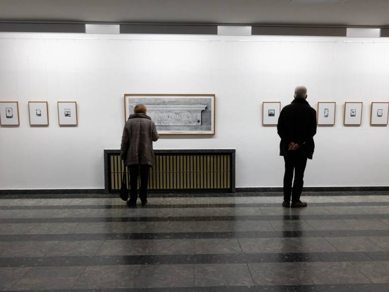 Zwei Personen schauen sich Bilder von Christian Retschlag im Regionshaus an.