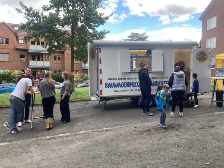 Bauwagen der DJE Hannover sowie Menschen an Stehtischen