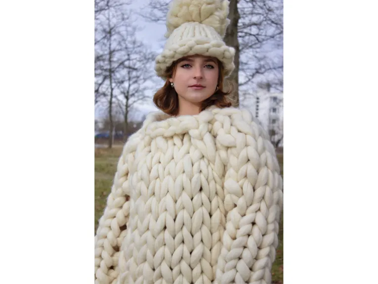 Eine Frau in Strickpulli und Strickmütze, beides hergestellt aus riesigen Maschen.